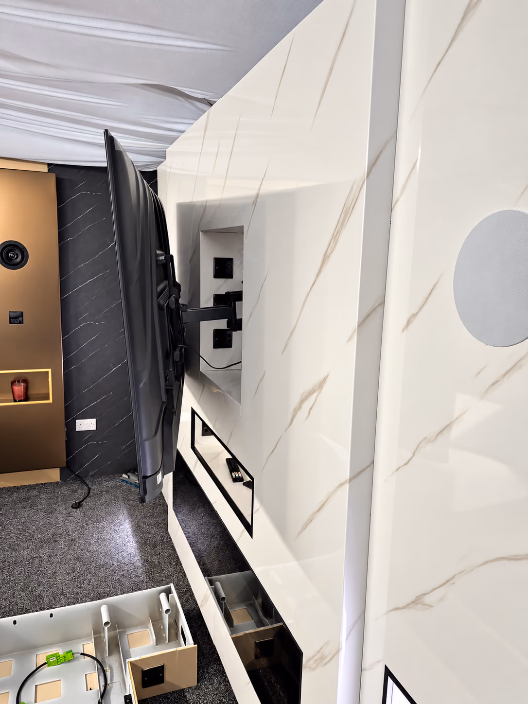 White and gold marble media wall during installation, with the TV swung out to show recessed sockets and a cable drawer below