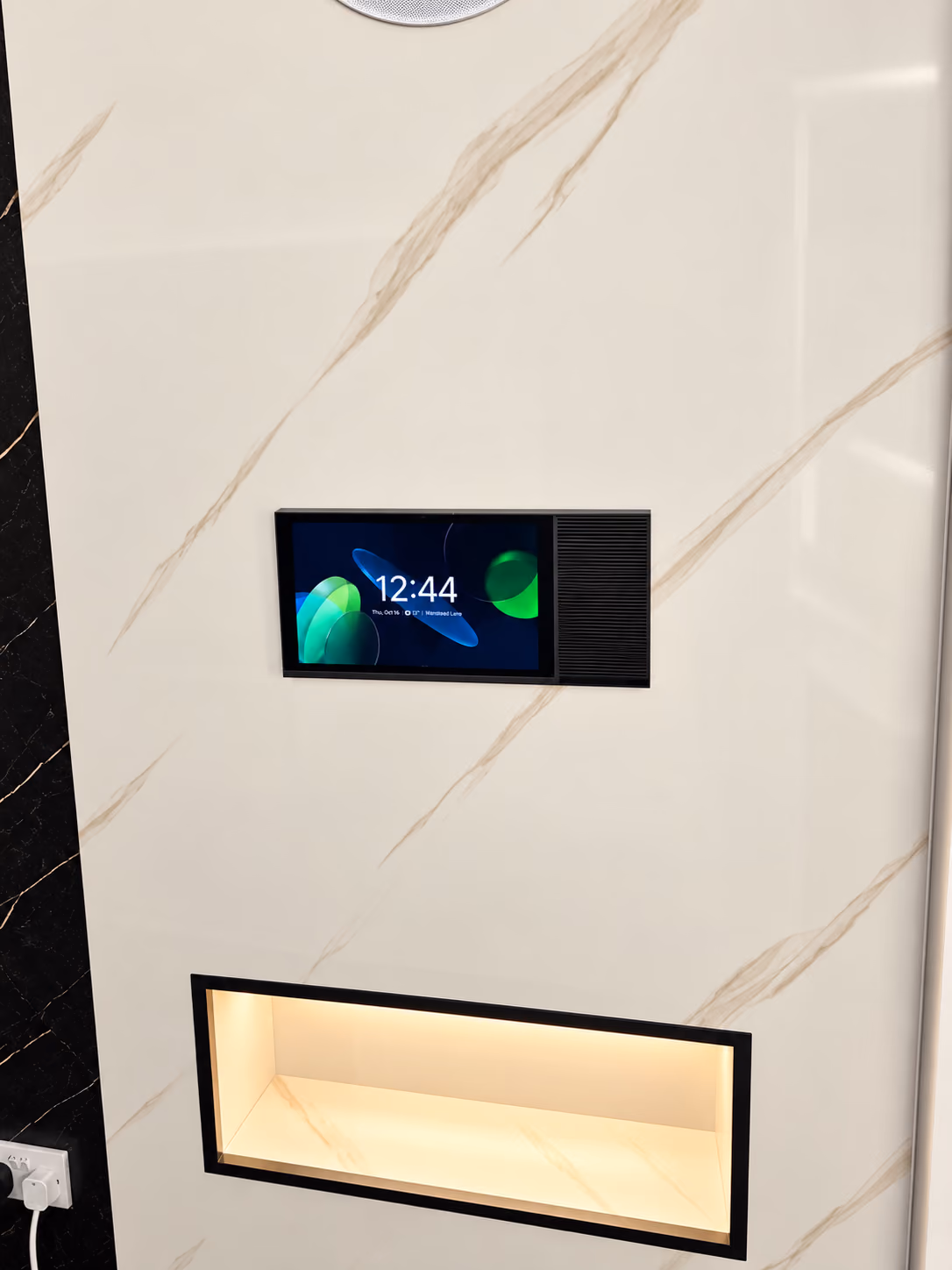 Smart home display panel showing the time, set flush into white marble above a warm lit display niche