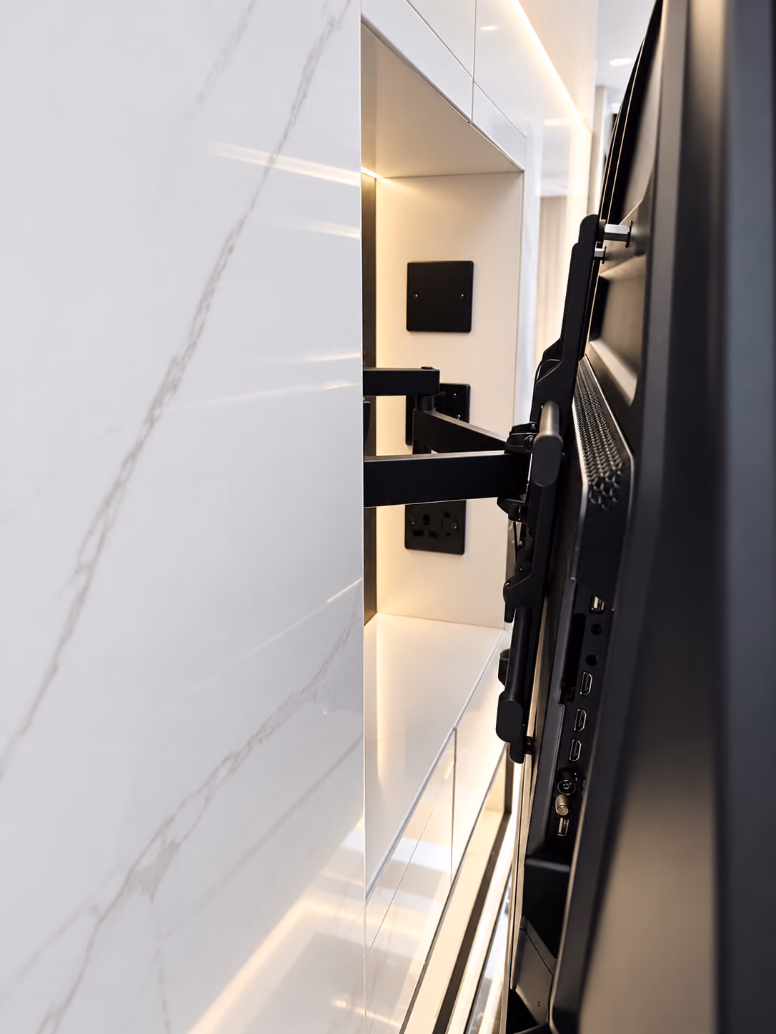 TV on a black swing-arm bracket pulled out from a white marble media wall, showing the sockets hidden in a lit recess behind it