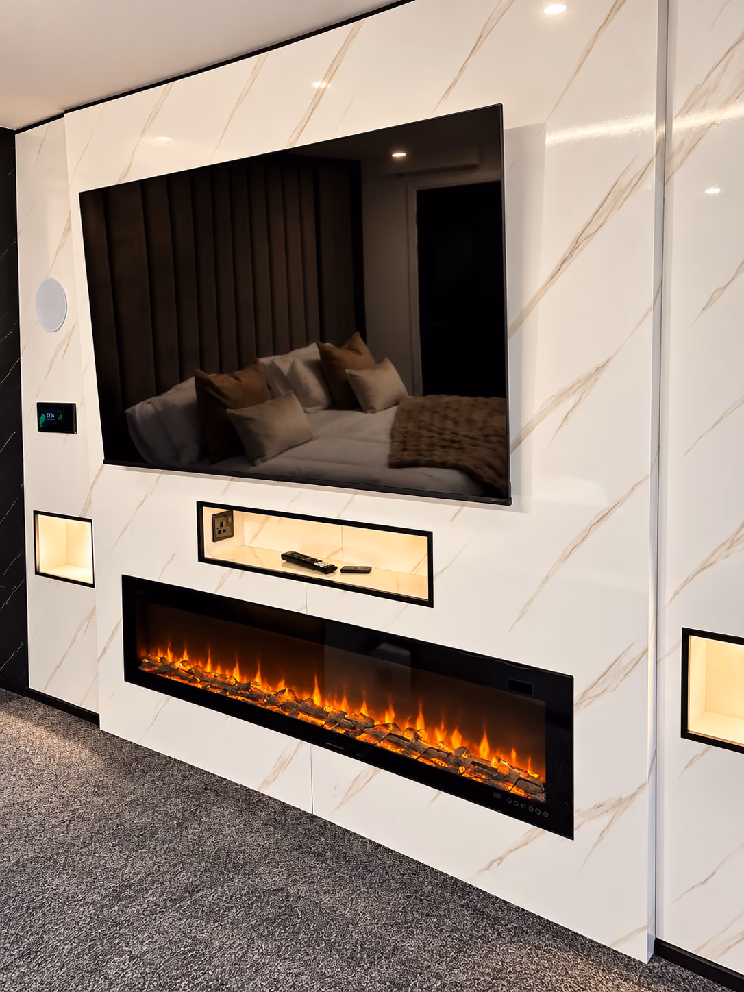 White and gold veined marble media wall with a wall-mounted TV, a lit shelf, a wide electric fire and lit side niches